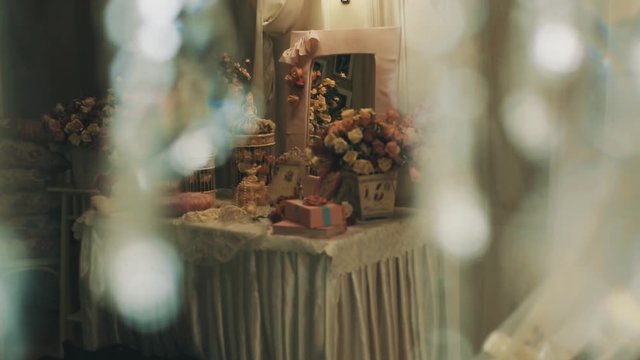 Girlish table with mirror, flowes, toys, presents and bird cages beyond glass chandelier particles in photo studio, close up