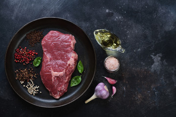 Top view of a frying pan with raw fresh ribeye beefsteak on a scratched metal background. Horizontal shot with copyspace