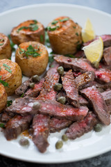 Closeup of italian beef tagliata with olive oil, capers, paprika, lemon and baked potato, studio shot