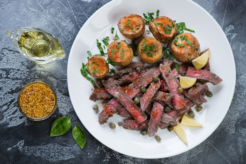 Above view of a white plate with grilled tagliata steak and baked potatoes