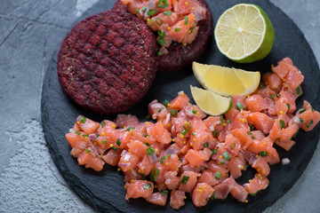 Close-up of salmon tartar with beetroot cutlets on a stone slate tray