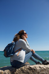 young woman sitting by seaside listening to music with headphones