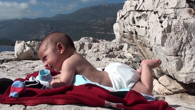 Baby in nappies sunbathing on rock at the seaside