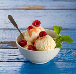 Tasty vanilla ice scoops with strawberry jam and mint in bowl on blue wooden rustic table. Closeup.