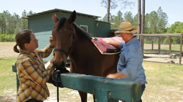 Farmer puts saddle pad on horse