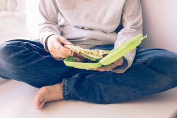 Boy sitting by the window holding a container with sweet sandwiches