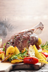 Pork knuckle baked with potatoes  on a wooden board. Italian cuisine. Selective focus.