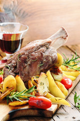 Pork knuckle baked with potatoes  on a wooden board. Italian cuisine. Selective focus.
