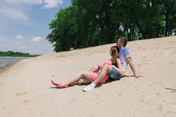 Young couple hugging and smiling at each other on the river bank. Walking along the sandy beach