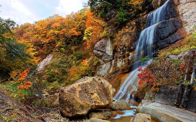 A silky waterfall in a mysterious gorge with colorful autumn trees on the rocky cliff between Yamagata & Miyagi, Japan ~ Nature scenery of Japanese countryside in beautiful fall season (Long Exposure)