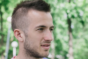 Fototapeta premium Portrait of a handsome young man in a clear sunny day. Green trees