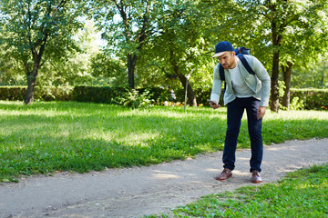 Fototapeta premium Concentrated young man walking down path and playing popular mobile game, full length portrait