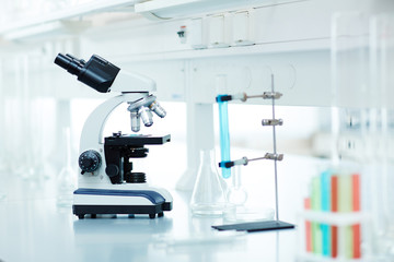 Electronic microscope and test tubes with colored liquid on table in modern empty laboratory