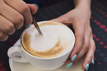 A very beautiful business woman sits in a cafe and holds a cup of coffee in her hands
