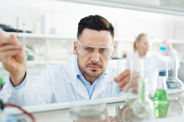 Portrait of focused scientist working on research in laboratory, performing chemical experiment dropping reactants into petri dish