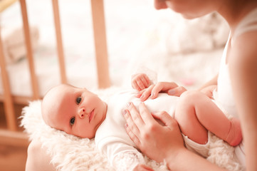 Cute baby girl lying on mothers hands indoors. Mother touching infant in room. Looking at camera. Motherhood. Maternity.