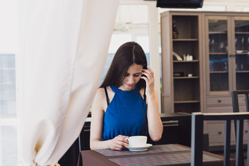 A very beautiful business woman sits in a cafe and holds a cup of coffee in her hands