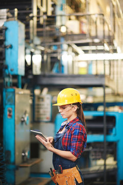 Profile view of female machine worker reading operational manual on digital tablet in order to carry out starting-up and adjustment works