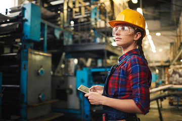 Waist-up portrait of female warehouse employee doing checklist with help of digital tablet, profile view