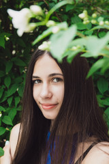 Fototapeta premium A very beautiful and cheerful girl stands on the street near a bush with white flowers