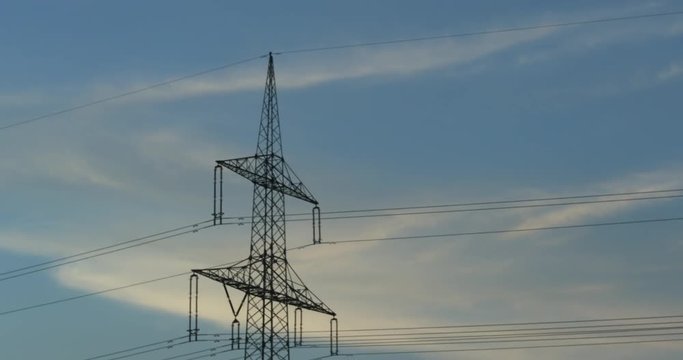 Handheld drive-by of a power supply line and a electricity pylon with a blue sky and cirrostratus clouds