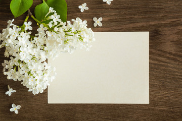 White lilac flowers with blank greeting card on the wooden table.