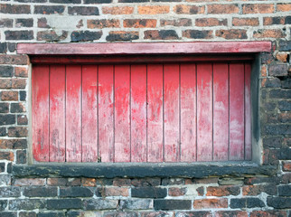 baorded up long window in an old victorian building with faded wood and peeling red paint