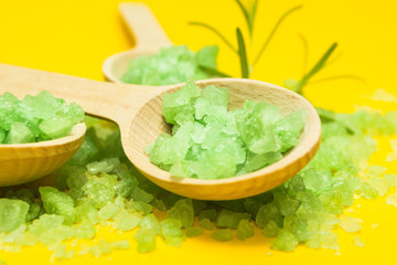 Green Salt in three wooden spoons on a yellow background. Vegetable ingredients for skin care.