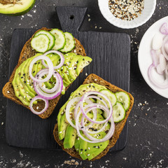 Sandwiches on toast grain dark bread with slices of avocado, sweet pink onions and multi-colored sesame seeds. Top view