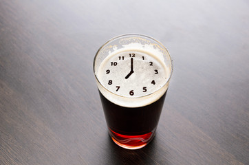 Clock silhouette on foam in beer glass on black table, view from above.