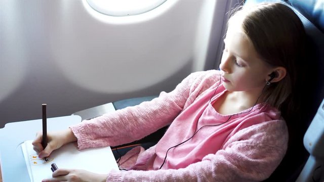 Adorable little girl traveling by an airplane. Kid drawing picture with colorful pencils sitting near window