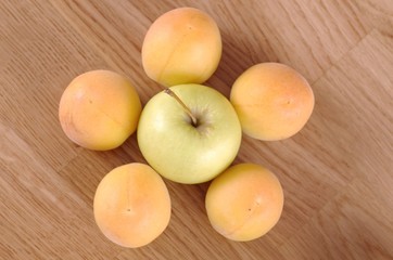 Apricots and apple on a wooden table.