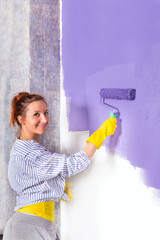 woman paints white wall with purple paint roller