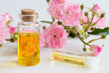 A bottle of rose essential oil with small rose blossoms