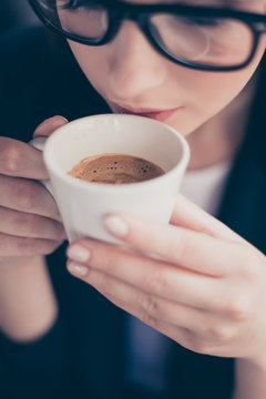 Great beginning of the day! Cropped close up photo of relaxed business lady, resting at her work place and drinking coffee, wearing black glasses