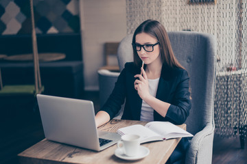 Portrait of serious young entrepreneur lawyer in formal wear and glasses, sitting at her work place in a coworking and thinking with a pencil in a hand