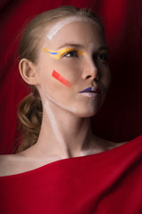 Girl with color make-up on a red background. Portrait of a blonde with a color make-up on a background of red cloth close-up.