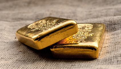 Two cast gold bars weighing 250 grams against the background of the texture of coarse cloth. Selective focus.