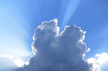 Sun rays look out behind of cumunus clouds in a blue sky
