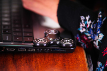 Young woman working in the computer and a popular fidget spinner toy over the laptop, on office...