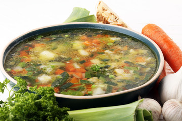 Broth with carrots, onions various fresh vegetables in a pot - colorful fresh clear spring soup. Rural kitchen scenery vegetarian bouillon or stock