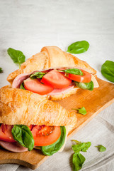Light and hearty spring breakfast. Croissant with ham, cheese, fresh tomatoes and basil. On a white stone table, with the ingredients. Copy space