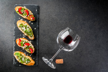 Italian food. Snacks. Antipasto. Bruschetta with pesto sauce, parmesan cheese, tomatoes and fresh basil. On black table, on slate board. With glass of red wine. Top view copy space selective focus