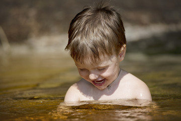 a little boy bathes in the lake and smiles
