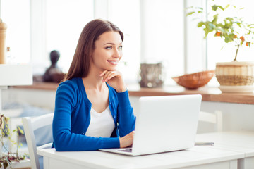 Young attractive lady is dreamy, browsing on her laptop in the cafe. She is in casual outfit, smiling, looking far in the window