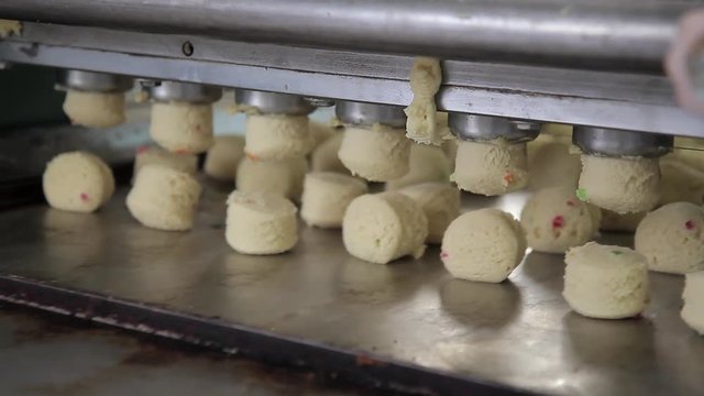 Same pieces of dough fall onto conveyor from dough feeder in bakery. Device continuously forms round pieces of ready-made sticky mass made from wheat flour, eggs and sugar with addition of candied