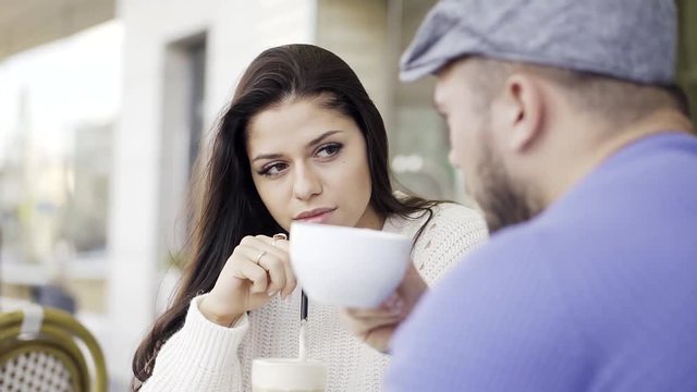 Close-up view of a girl in love sitting outside in cafes. The man gives the girl to smell the aroma of his black coffee.