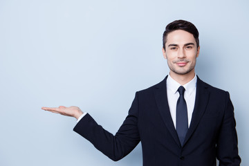 Cheerful handsome smiling banker guy with stubble is holding the copy space. He is wearing formal wear and a tie, stands on a light background