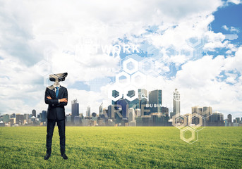 Camera headed man standing on green grass against modern citysca