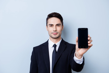 Handsome young guy finance broker with stubble is holding phone with black screen. He is wearing formal wear and a tie, stands on a light background